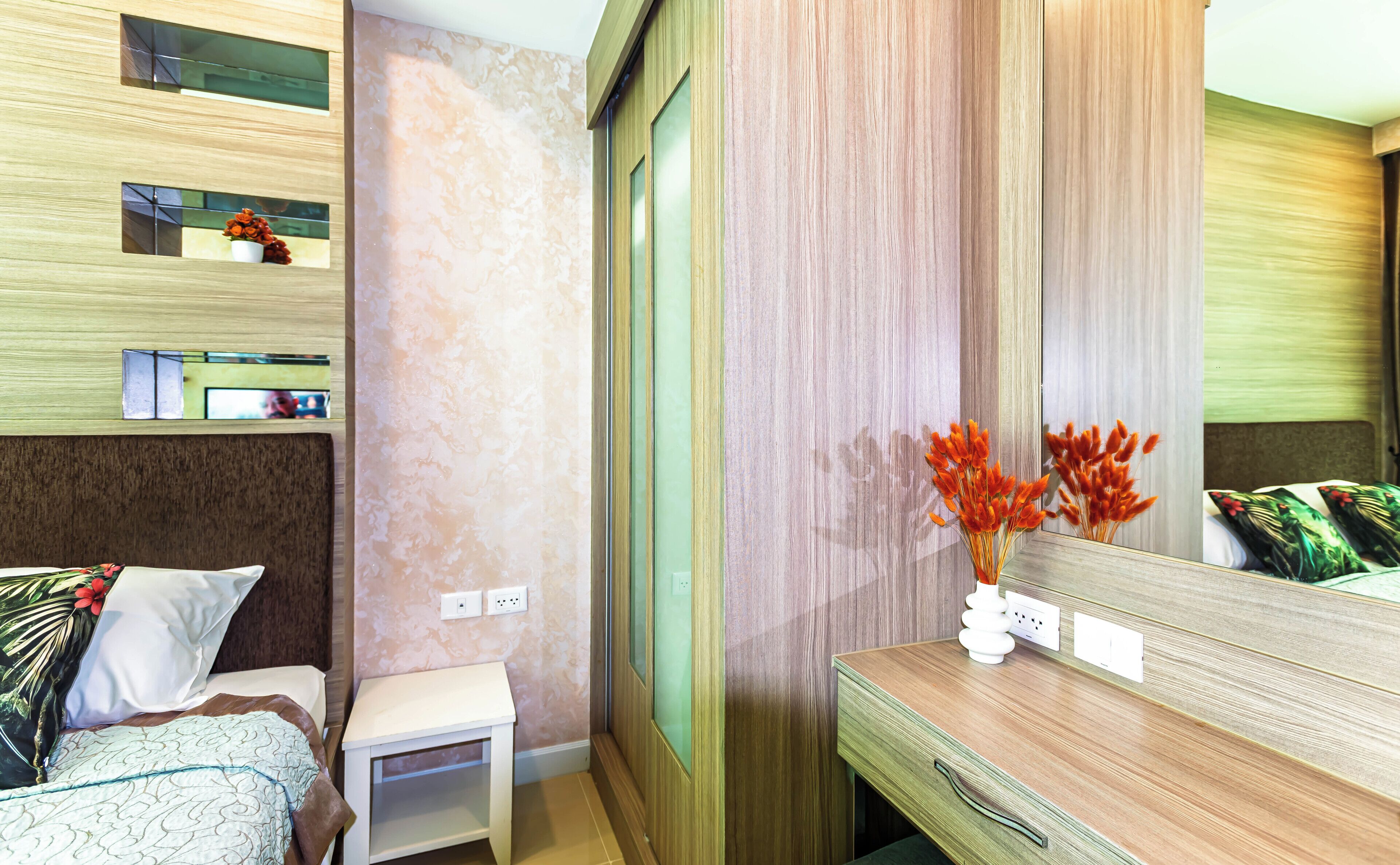 A hotel room with a bed, bedside table, mirror, and a wall with a textured pattern.