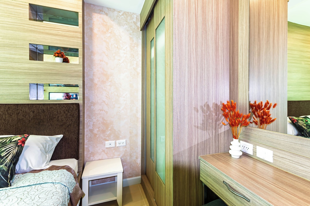A hotel room with a bed, bedside table, mirror, and a wall with a textured pattern.
