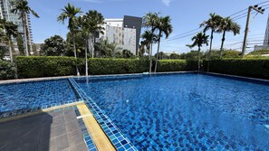 Ein Swimmingpool mit Fliesenrand, umgeben von Palmen und einer Hecke.