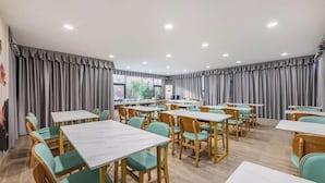 A dining area with tables and chairs, a large window, and curtains. - Xana Lite Hotel (Guangzhou)