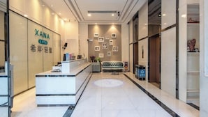 A hotel reception area with a reception desk, a sofa, and framed pictures on the wall. - Xana Lite Hotel (Guangzhou)