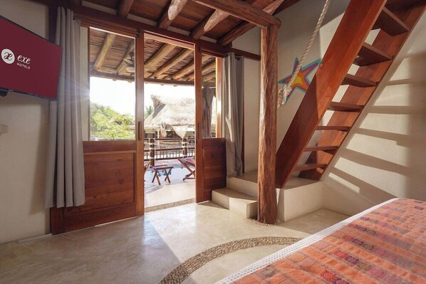 A hotel room with a wooden staircase, a large window with a view of the outside, and a bed with a patterned bedspread. - Hotel El Pueblito (Isla Holbox)