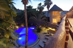 A pool area with lounge chairs and a thatched-roof building. - Hotel El Pueblito (Isla Holbox)