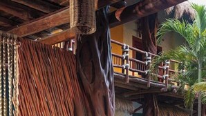An outdoor dining area with a wooden table and chairs, surrounded by a tropical setting with plants and a thatched roof structure. - Hotel El Pueblito (Isla Holbox)