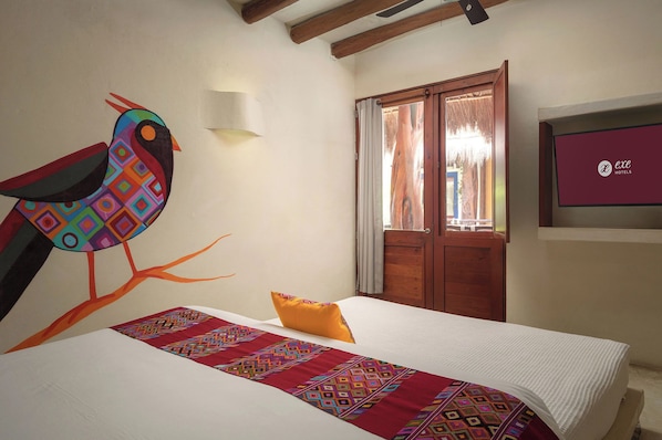 A hotel room with a bed, a colorful wall mural, a wooden door, and a TV screen displaying the hotel name. - Hotel El Pueblito (Isla Holbox)