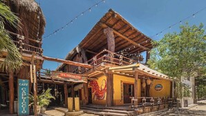 A rustic building with a wooden balcony, a sign for 'EL QUERETTO', and a 'CAFE CAPRICCIO' sign. - Hotel El Pueblito (Isla Holbox)