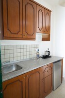 A kitchen with wooden cabinets, a stainless steel sink, a countertop, a kettle, and a bottle of water.