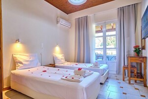 Habitación de hotel con dos camas, techo de madera, unidad de aire acondicionado, ventana con cortinas y una pequeña mesa con una planta.