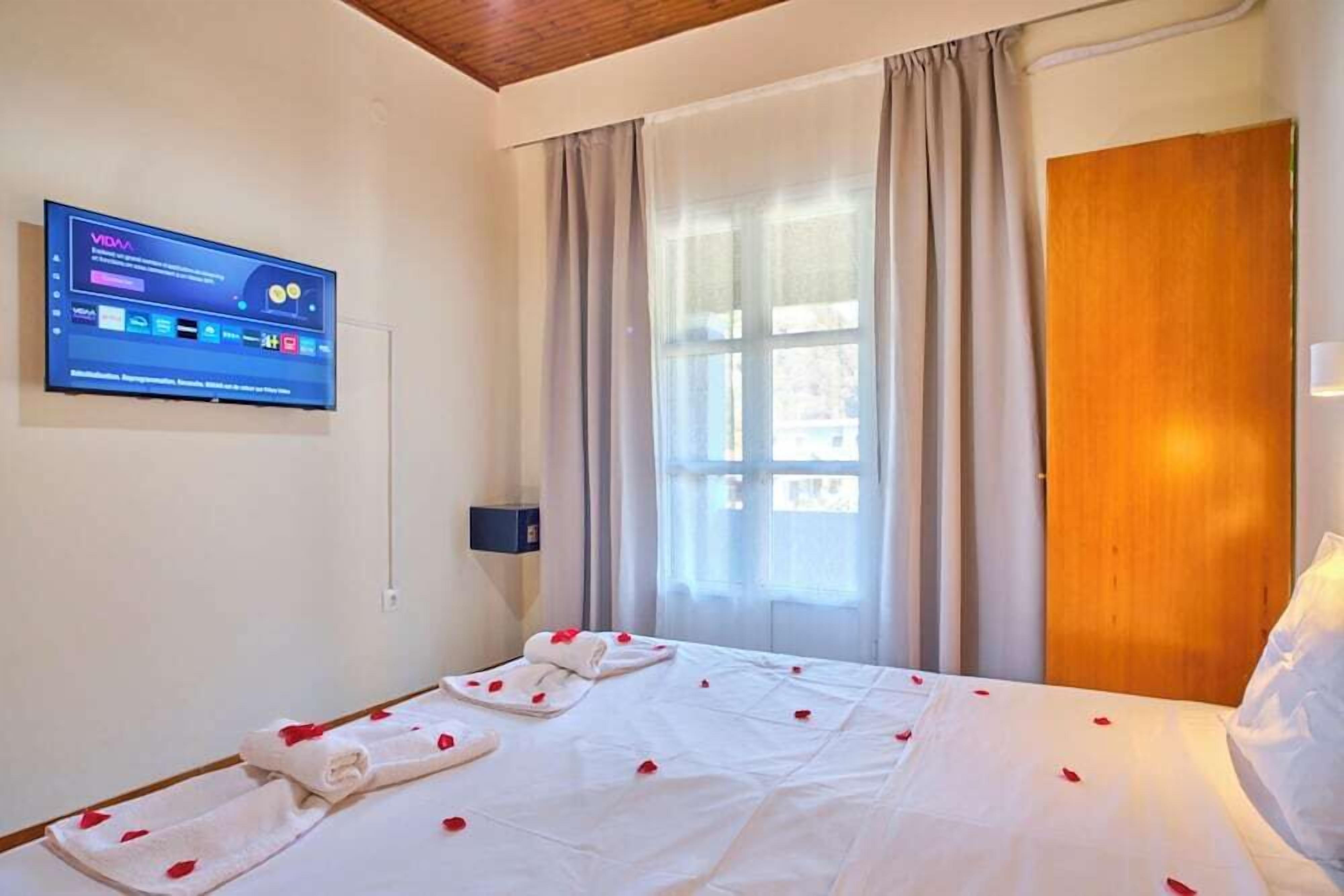 Una habitación de hotel con una cama, un televisor montado en la pared y una ventana con cortinas.