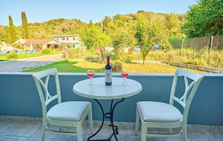 Un balcón con dos sillas blancas y una mesa, una botella de vino y dos copas sobre la mesa.