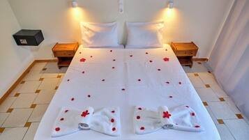 Ein Doppelbett mit weißen Leinentüchern und Rosenblüten, zwei Nachttische sowie eine wandmontierte Leuchte.