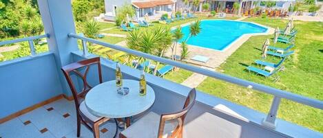 Varanda com mesa e cadeiras, com vista para uma piscina e vilas.