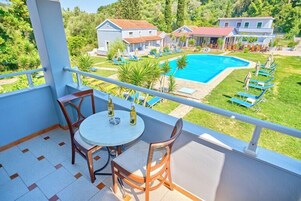 Un balcón con mesa y sillas, con vistas a una piscina y algunas villas.