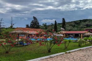 A hotel with a swimming pool, surrounded by lush greenery and a clear sky.