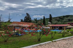 A hotel with a swimming pool, surrounded by lush greenery and a clear sky.
