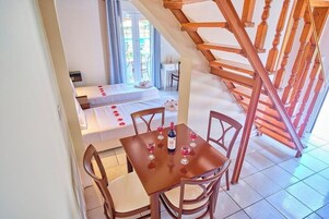 Una habitación con escalera de madera, una mesa de comedor con sillas y una cama con colcha blanca.