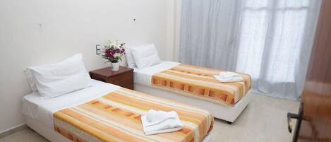 A hotel room with two beds, a nightstand, a vase with flowers, and a window with curtains.