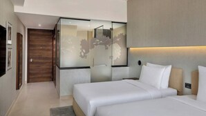 Habitació d'hotel moderna amb llit, separador de vidre i panell de control fixat a la paret.
