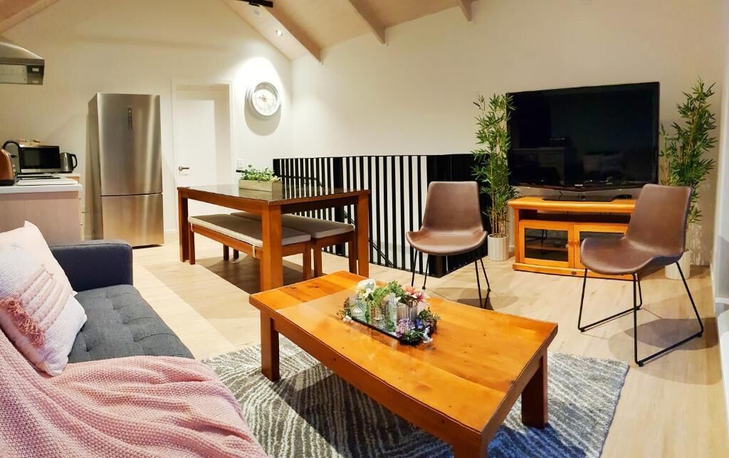 A modern living room with a sofa, a wooden coffee table, a TV, and a kitchen area with a refrigerator and microwave.