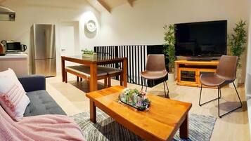 A modern living room with a sofa, a wooden coffee table, a TV, and a kitchen area with a refrigerator and microwave.