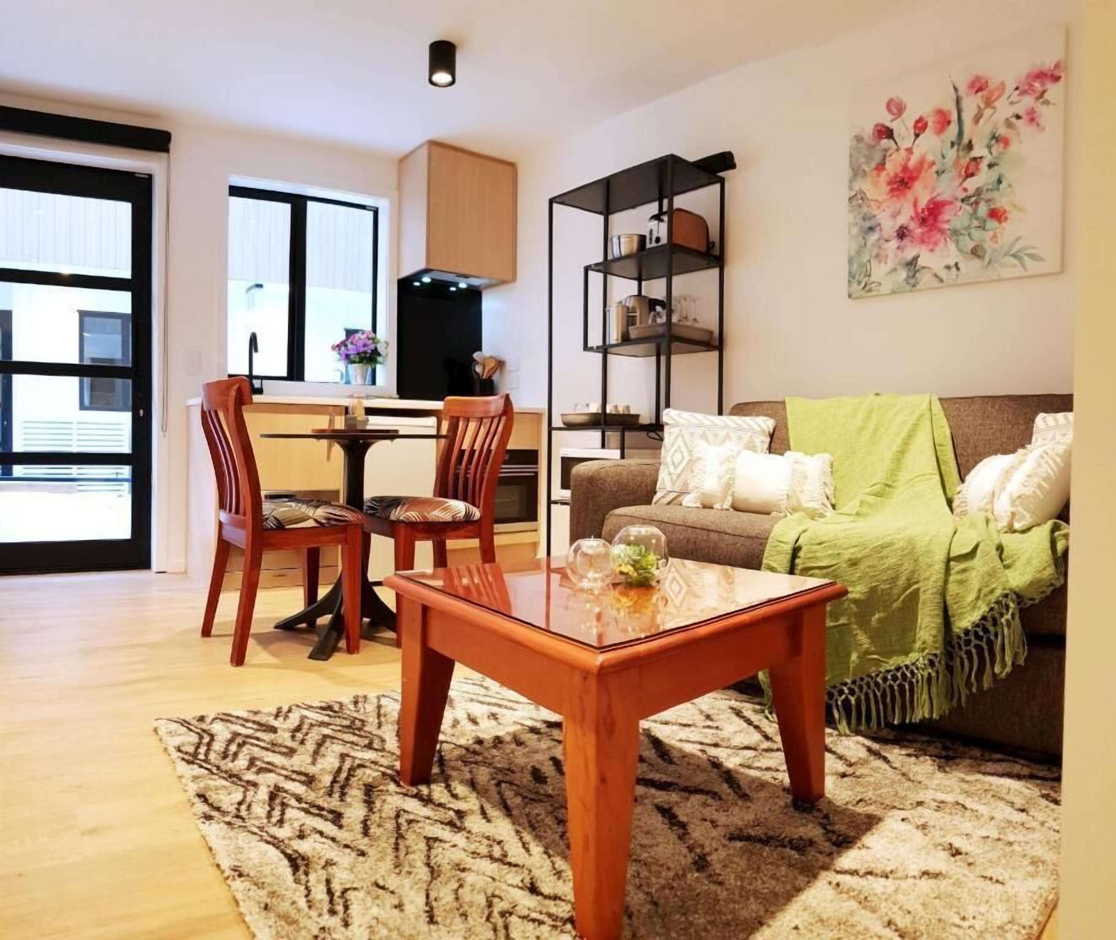 Een woonkamer met een houten salontafel, een bank met een groene plaid en een boekenkast.