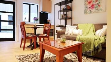 Een woonkamer met een houten salontafel, een bank met een groene plaid en een boekenkast.