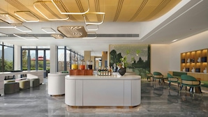 Eine moderne Hotelhalle mit einer zentralen Rezeption, einer Lounge und großen Fenstern mit Blick auf Grünflächen.