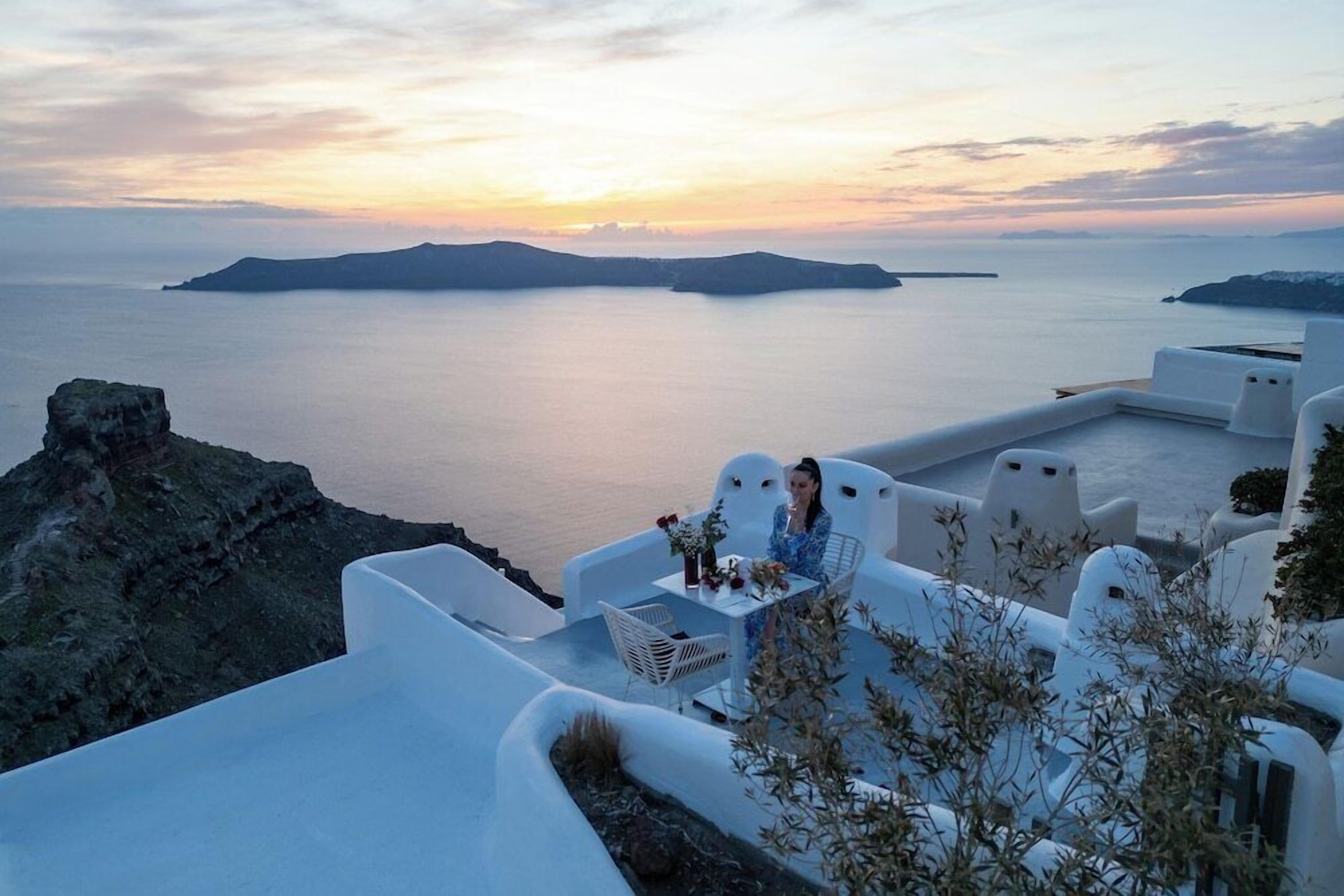 Una terrazza con mobili bianchi che si affaccia su uno specchio d'acqua e un'isola in lontananza.