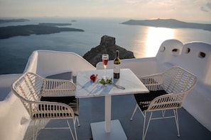 Una mesa con dos sillas blancas, una botella de vino y una copa de vino en una terraza con vista a un cuerpo de agua.