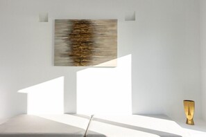 Una habitación minimalista con un cuadro abstracto grande, una silla moderna y una pequeña mesa.