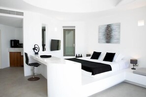 A modern hotel room with a white bed, a desk, and a chair. - Heavens Edge Cliffside Villas & Suites (Santorini)