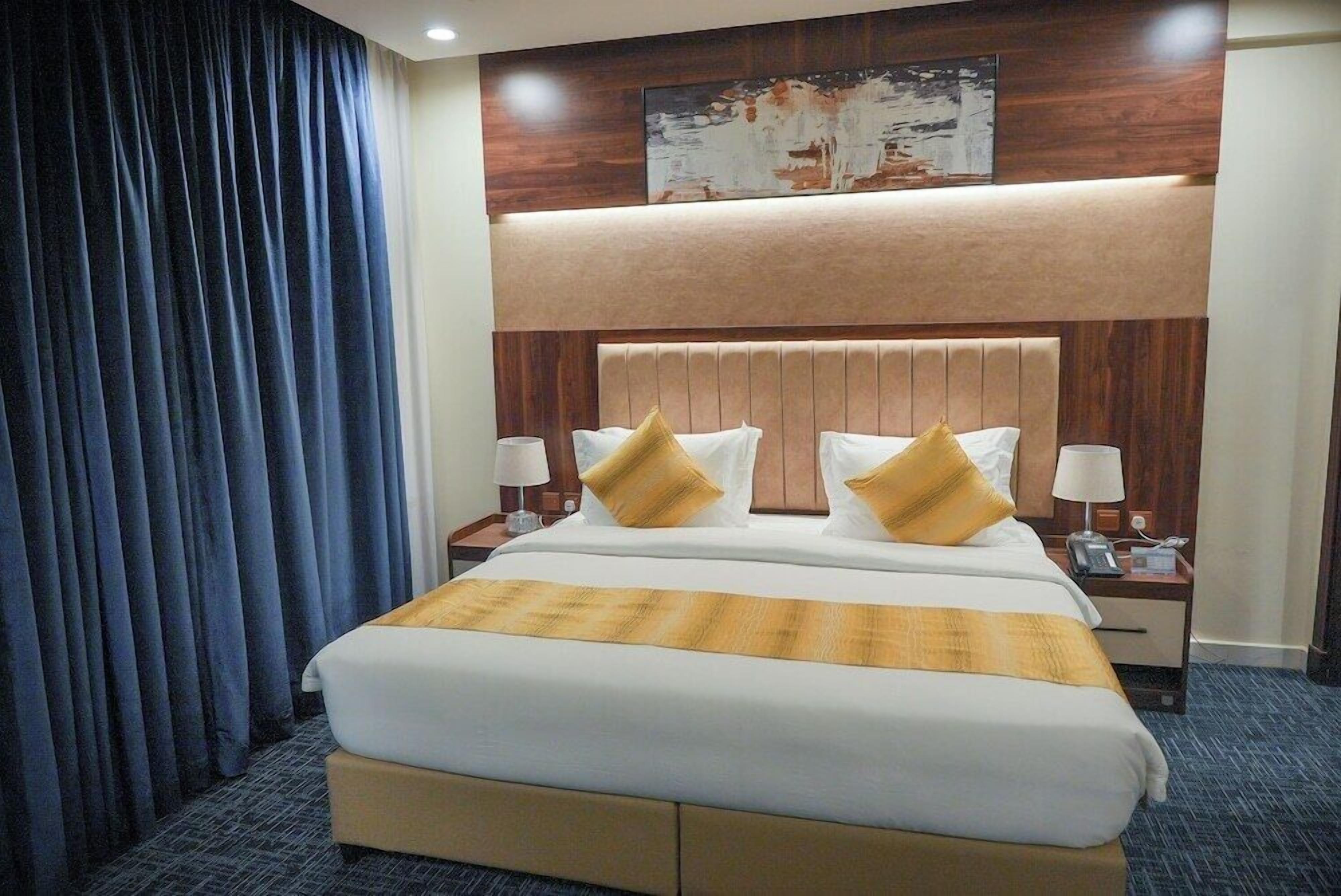 A hotel room with a large bed, two bedside tables, a headboard, and a wall-mounted artwork.