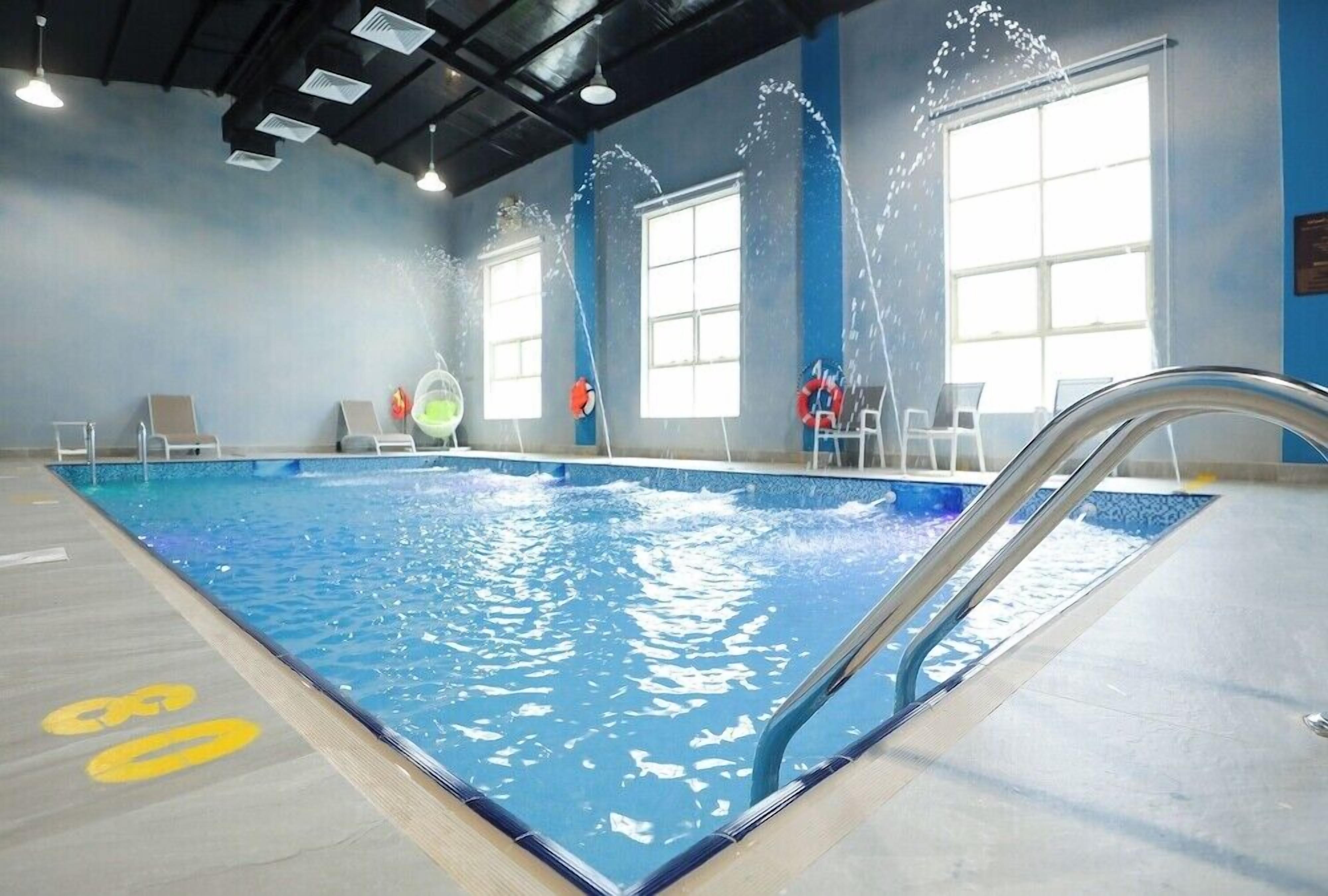 An indoor swimming pool with clear water, a diving board, and safety equipment.