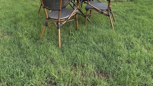 An outdoor seating area with wicker chairs and a table, a fountain, and a modern building in the background. - Al Mada Arabia Hotel (Jizan)
