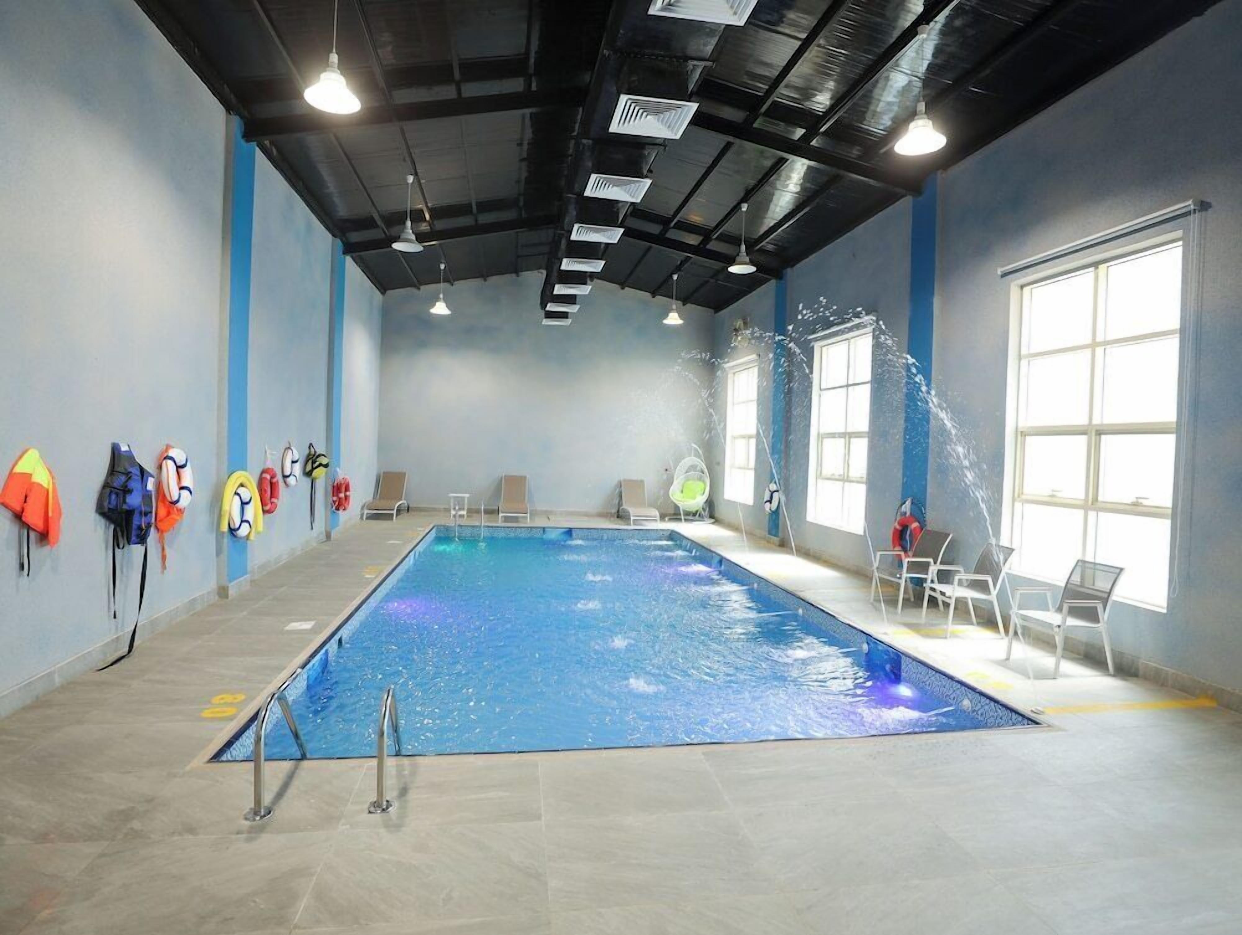 An indoor swimming pool with clear water, surrounded by lounge chairs and life jackets on the walls.