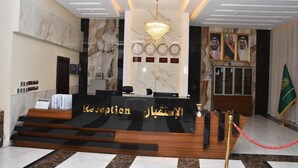 A reception area with a marble wall, a chandelier, a reception desk, and a flag. - Al Mada Arabia Hotel (Jizan)
