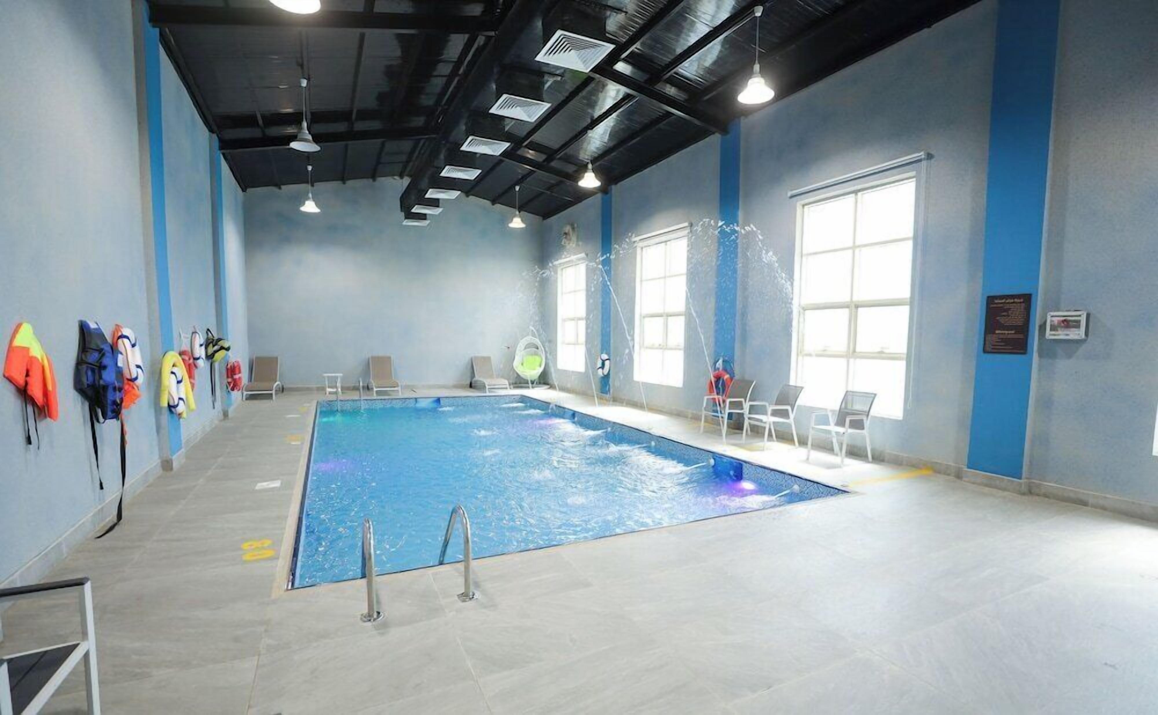 An indoor swimming pool with clear water, surrounded by walls with blue and white patterns, and a ceiling with visible beams and lighting fixtures.