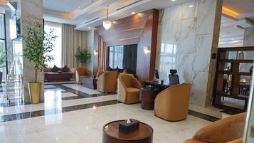 A lobby with a marble floor, seating area with sofas and armchairs, a reception desk, and a large plant.