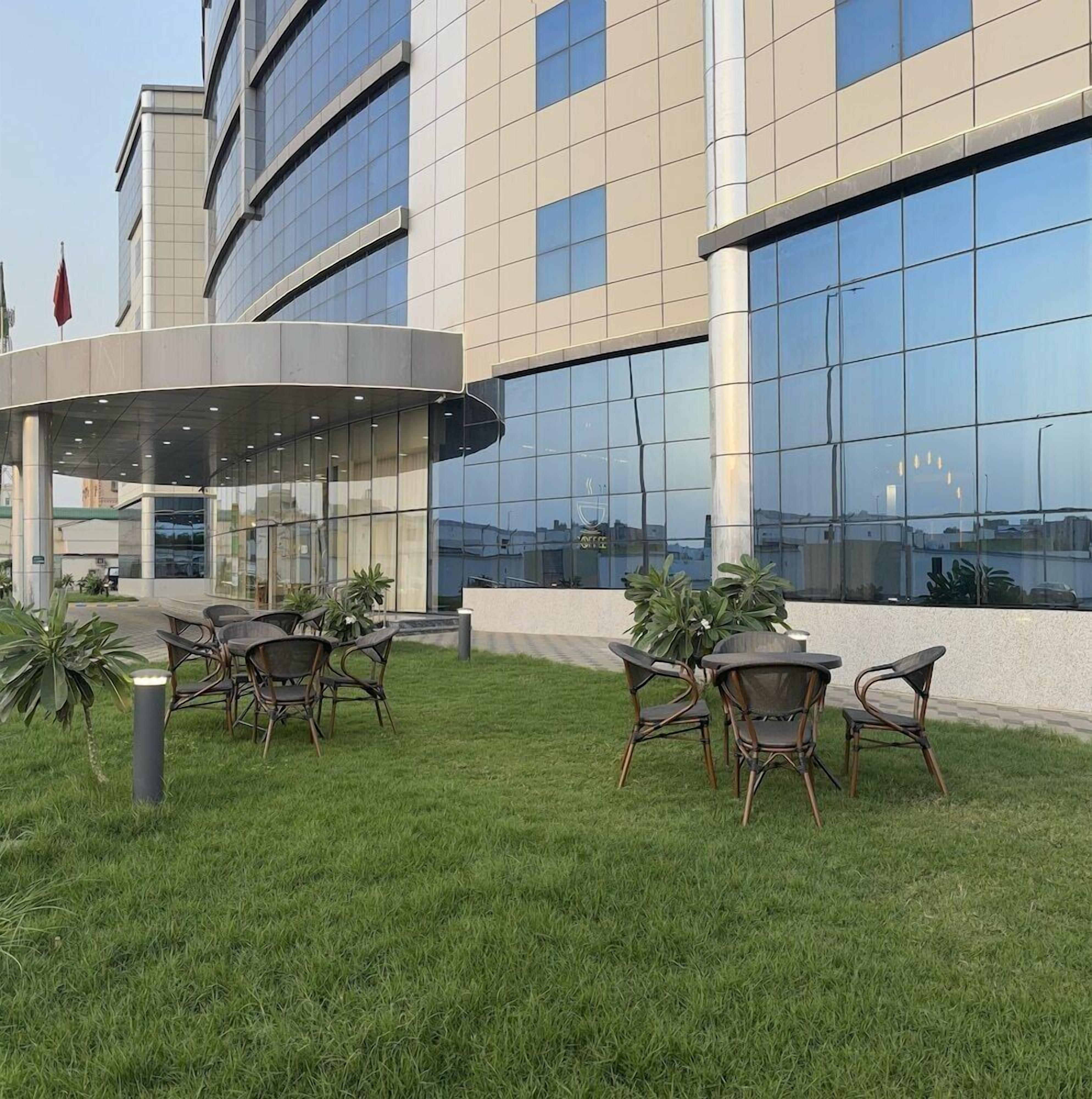 A modern building with a glass facade, outdoor seating area with wicker chairs, and a flagpole.