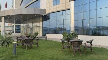 A modern building with a glass facade, outdoor seating area with wicker chairs, and a flagpole.