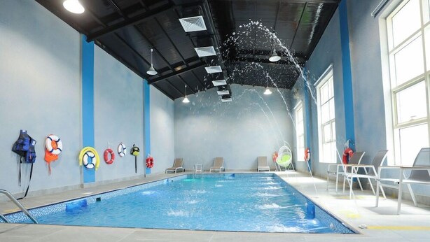 An indoor swimming pool with a clear water surface, surrounded by lounge chairs and life-saving equipment on the walls. - Al Mada Arabia Hotel (Jizan)