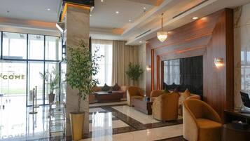 A hotel lobby with a reception desk, seating area, and large windows.