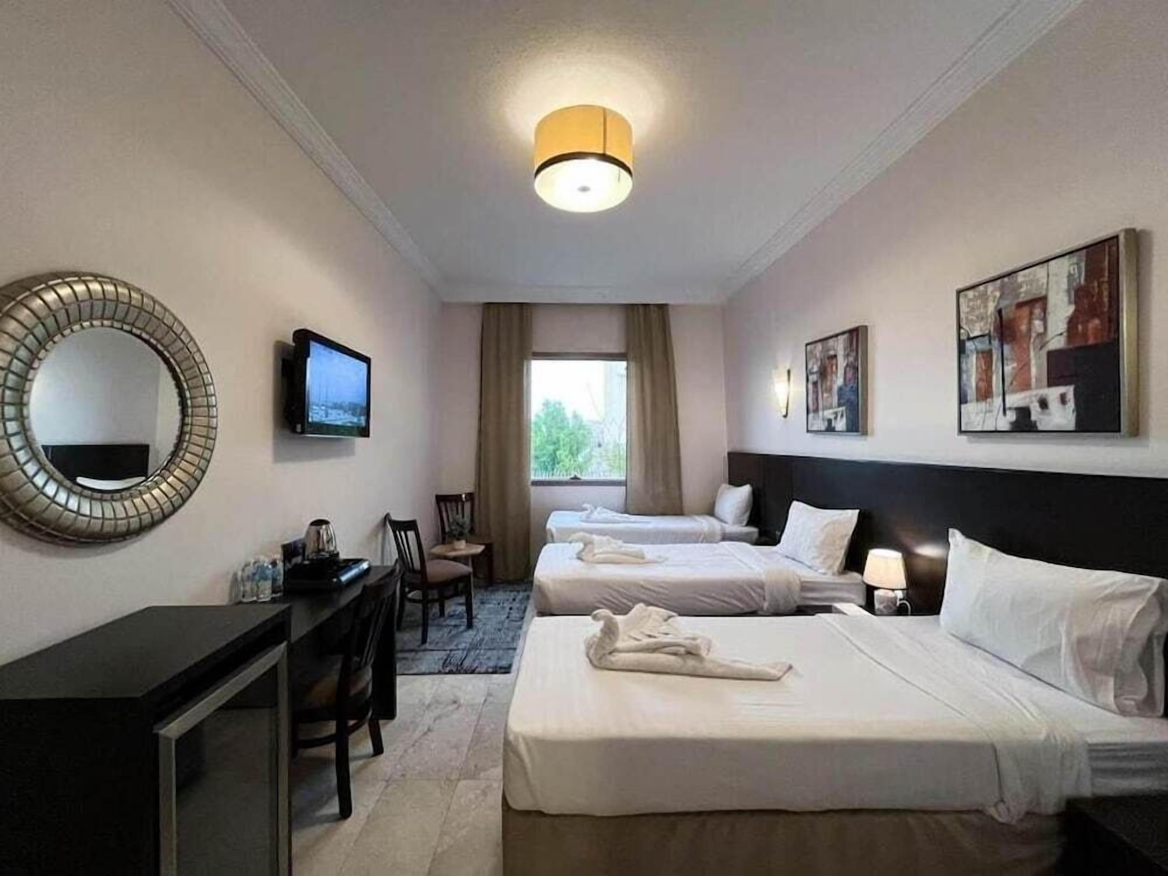 Une chambre d’hôtel avec deux lits, un bureau, une chaise, une télévision et des œuvres d’art accrochées aux murs.