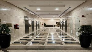 Un couloir d’hôtel avec un sol à motifs à carreaux, un extincteur et des plantes en pot.