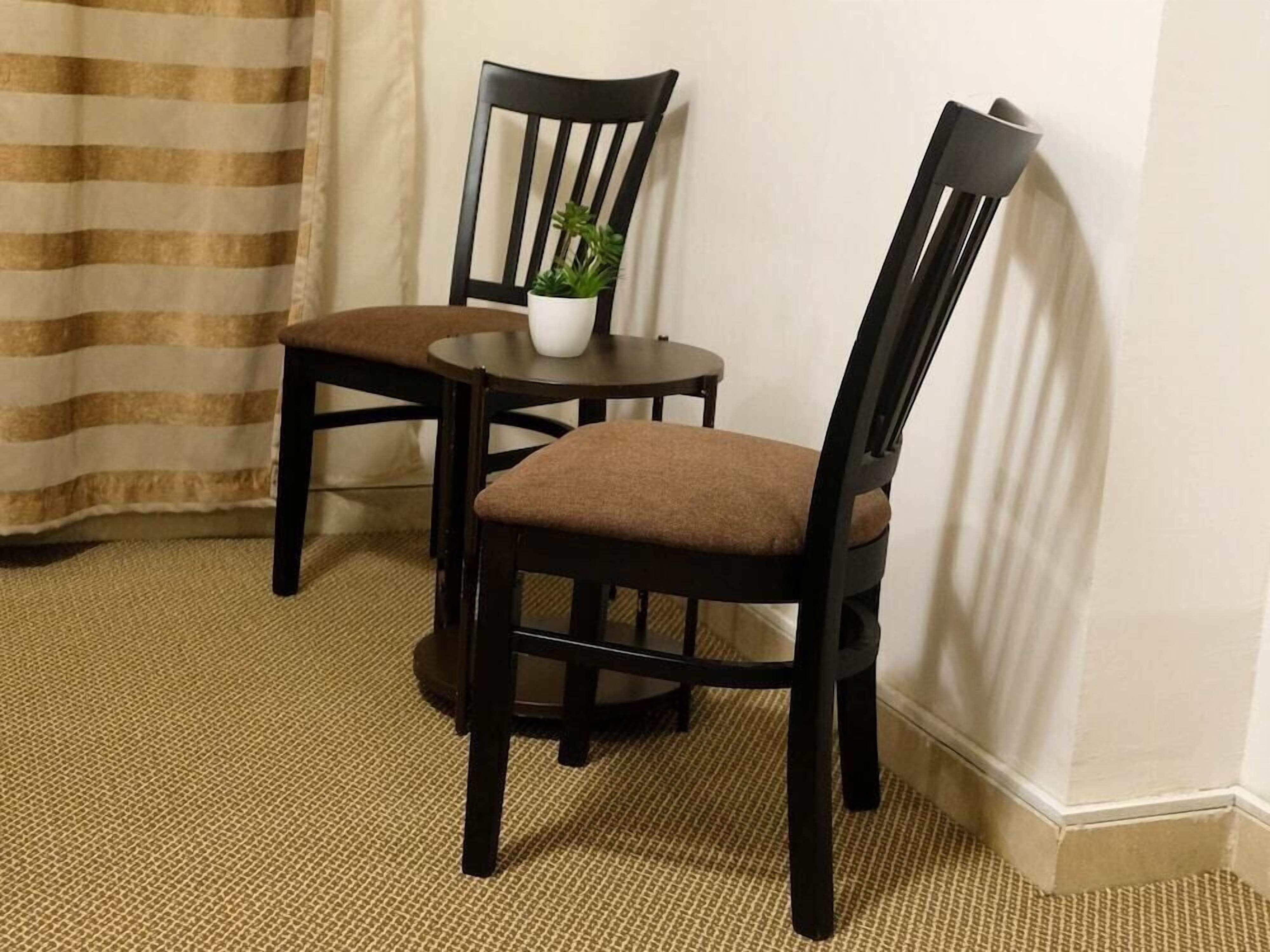 Une pièce avec deux chaises en bois foncé, une petite table ronde et une plante en pot.