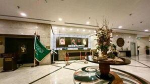 Un hall d’entrée avec un comptoir de réception, un drapeau, une plante décorative et un sol à motifs.