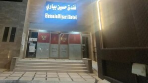 L’entrée de l’hôtel Hussain Biyari, avec une enseigne en arabe et en anglais, un escalier menant à l’entrée et une façade moderne.