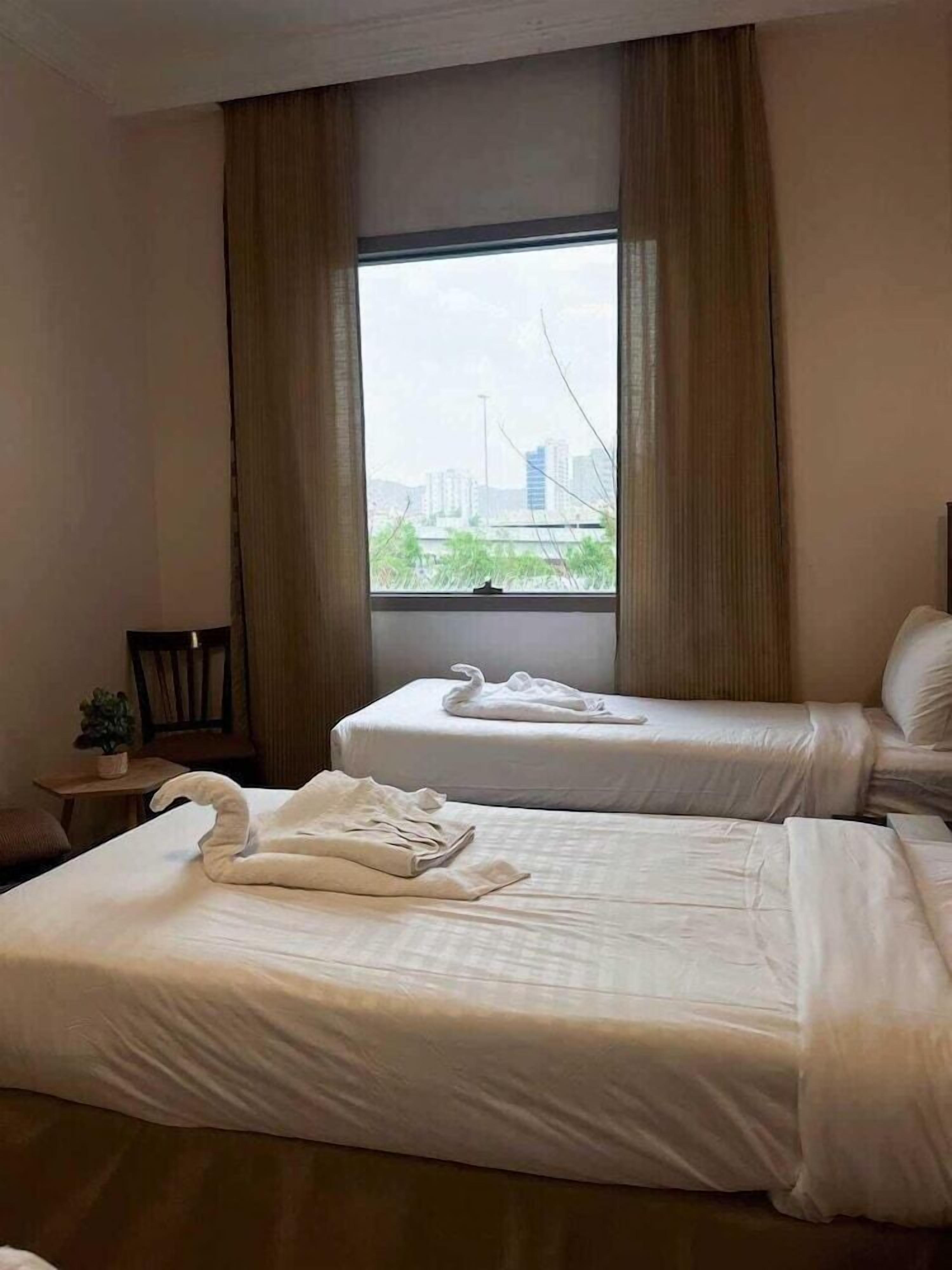 Habitación de hotel con dos camas, una ventana con cortinas, una silla y una mesita con una planta.