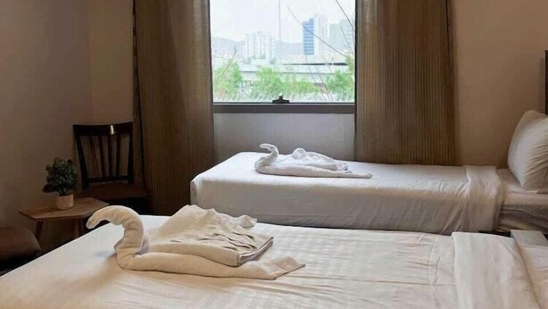 Une chambre d’hôtel avec deux lits, une fenêtre avec des rideaux, une chaise et une petite table sur laquelle est posée une plante.
