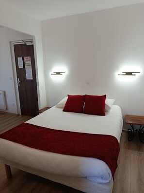 A hotel room with a bed, a wooden bench, and two wall-mounted lights.
